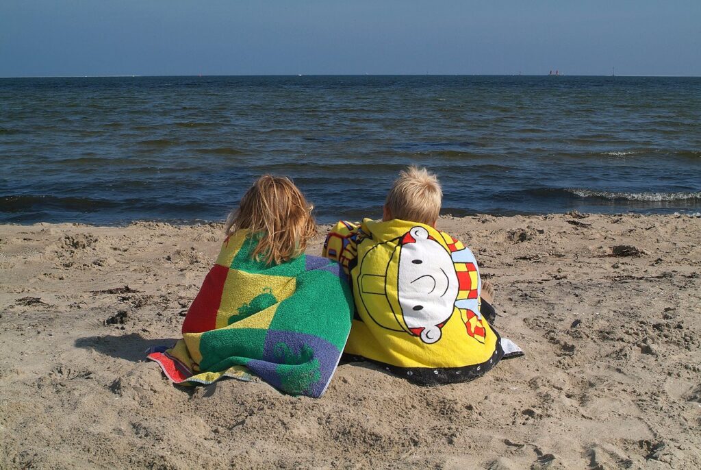 To børn sidder på stranden med håndklæder