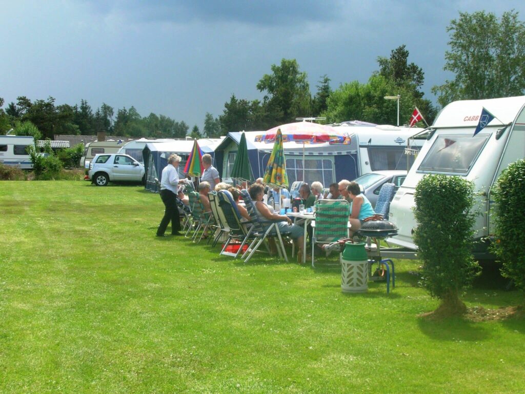 Folk nyder sommerdag på campingplads med campingvogne